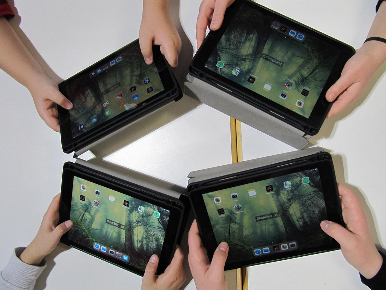 Vier Tablets im Kreis gehalten von vier Handpaaren