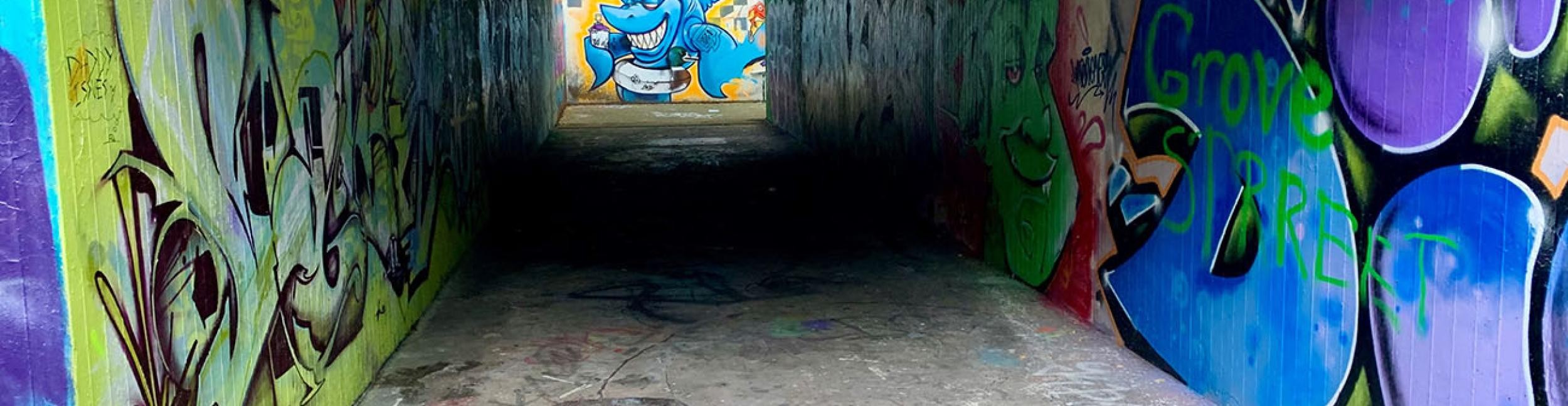 Underpass with colorful graffiti on the walls - letters, green face, blue shark with swimming ring