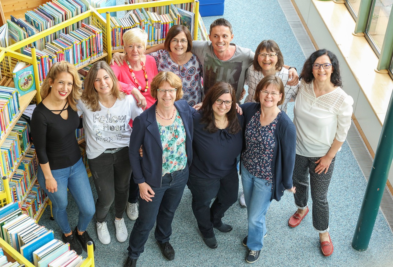 Photo de groupe des collaborateurs de la bibliothèque municipale, 10 femmes et 1 homme, en arrière-plan des étagères avec des livres. 