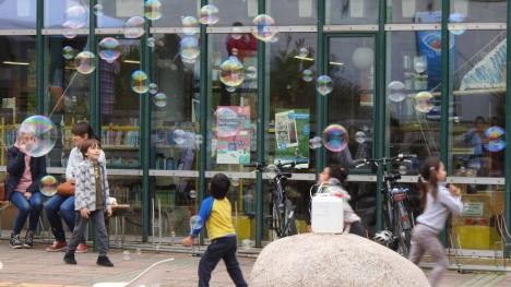 Enfants faisant des bulles de savon devant la bibliothèque - Lien vers la page Engagement pour les personnes en fuite