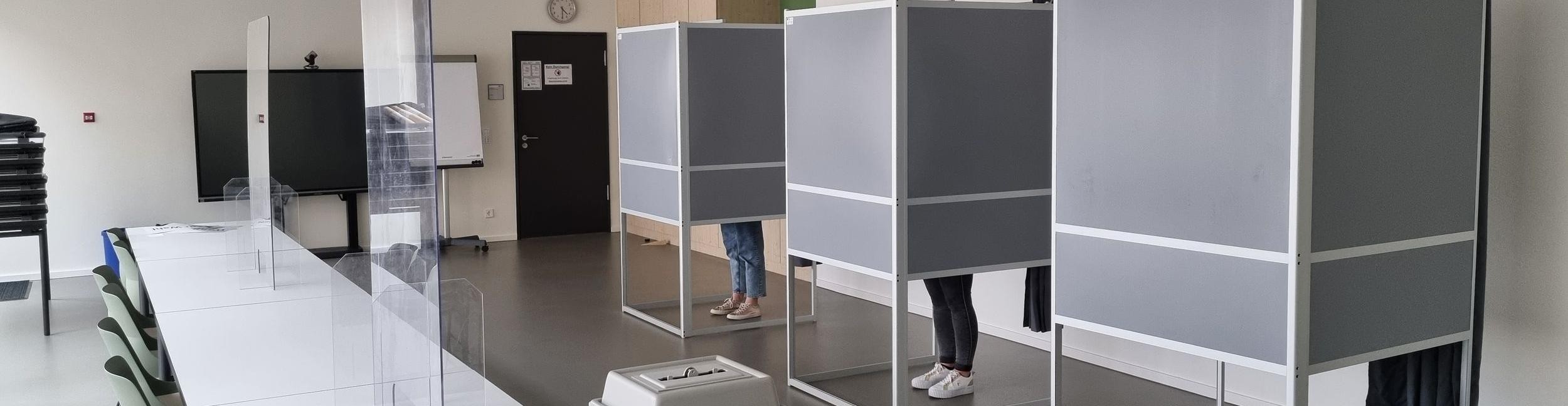 Des personnes se tiennent dans l'isoloir d'un bureau de vote
