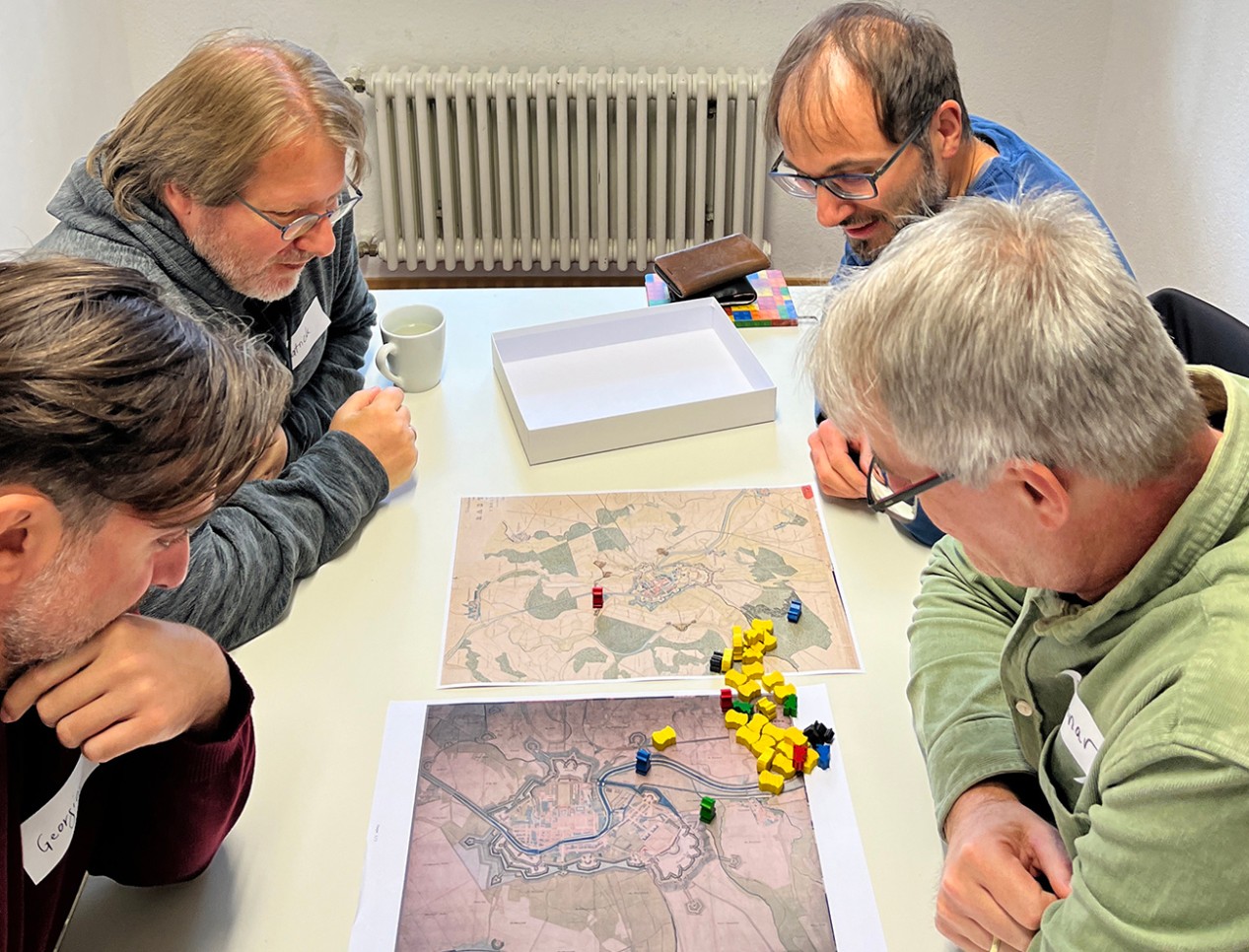 Als Spielfeld dient eine historische Karte von Rastatt. Foto: Stadt Rastatt/Birgitt Stellmach Teilenhmerinnen und Teilnehmer sitzen am Tisch und erfinden Brettspiel