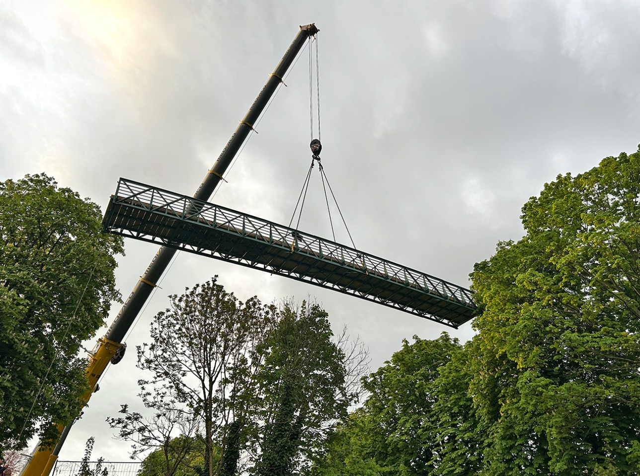 Der restaurierte Schachtelbachsteg wird an seinen ursprünglichen Platz gesetzt. Foto: Stadt Rastatt/Samira Kaiser Schachtelbachsteg schwebt an einem Kran über der Lücke, in der er hineingesetzt wird