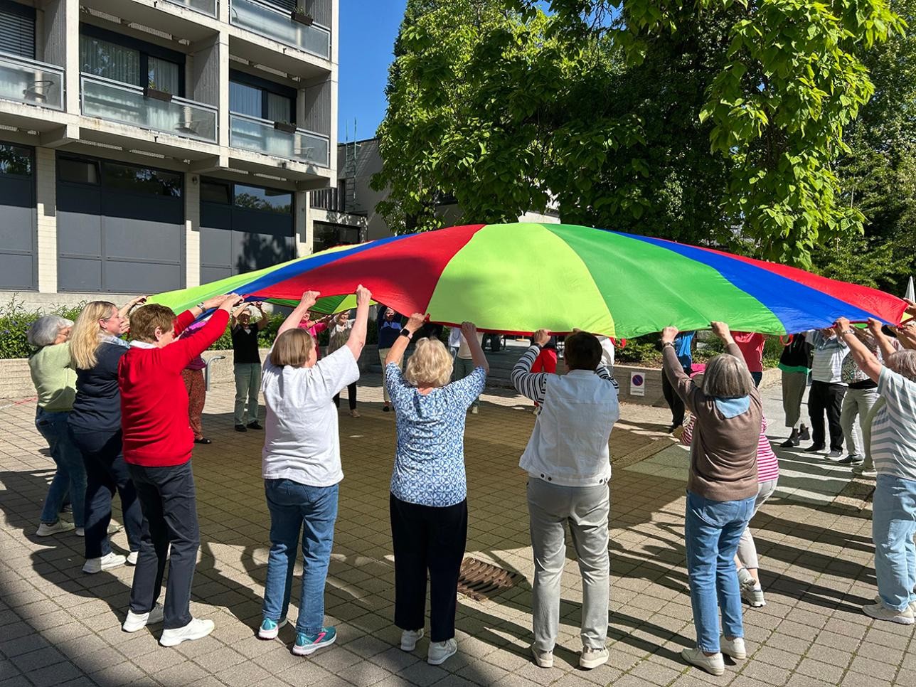 Gemeinsam machen die Seniorinnen und Senioren unter der Leitung von Petra Möller Bewegungsübungen im Freien. Foto: Samira Kaiser/ Stadt Rastatt Menschen halten zusammen einen Fallschirm und machen Sport
